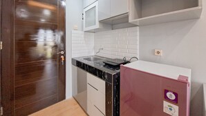 Eine kleine Küche mit einer dunkelbraunen Holztür, weißen Schränken, einer weißen Fliesenwand und einem rosa Kühlschrank.