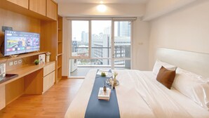 Een moderne hotelkamer met een groot bed, een televisie op een houten plank, en uitzicht op de stad.