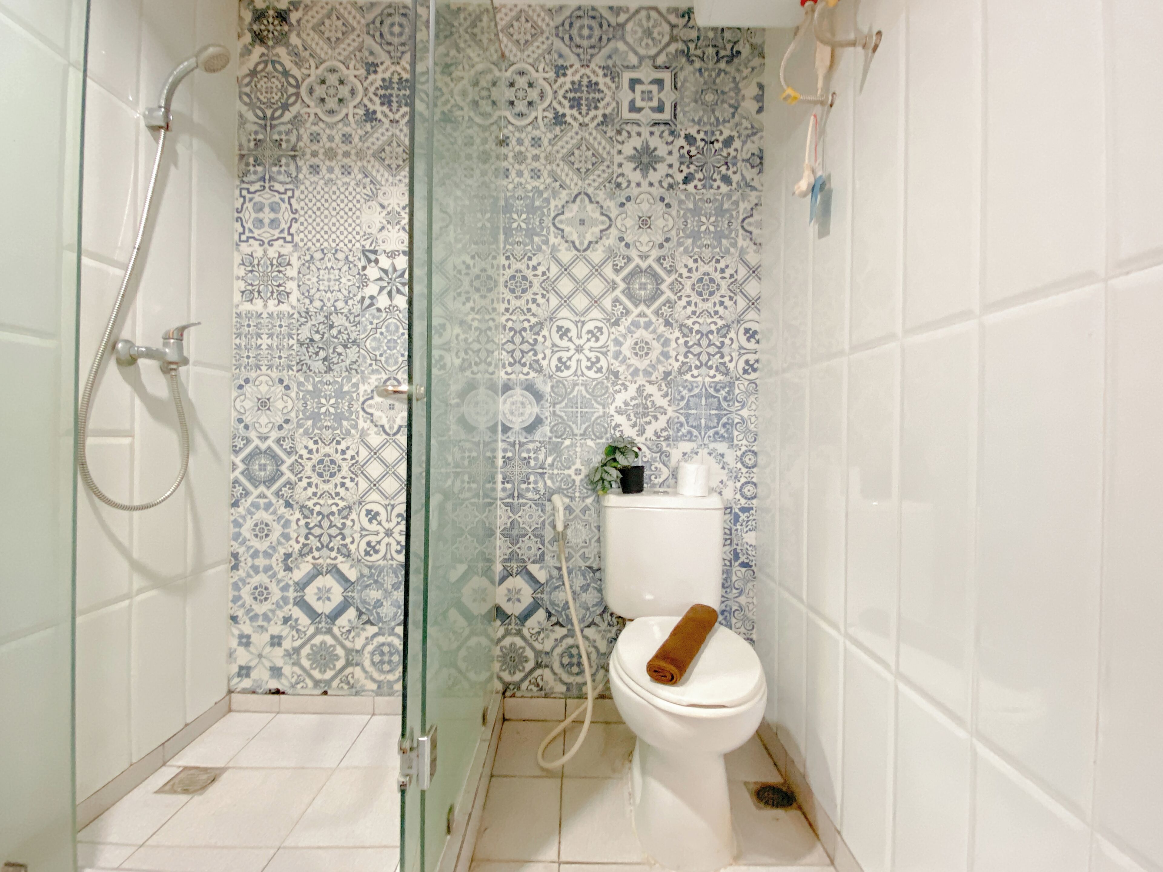 Un baño con baldosas estampadas, cabina de ducha de vidrio, inodoro con toalla y una pequeña planta en maceta.