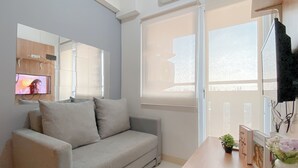 A modern living room with a grey sofa, a wooden coffee table, and a TV mounted on the wall. - Compact 2Br Apartment Direct Access To Mall At Green Pramuka City (Jakarta)