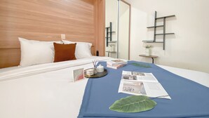 A neatly made bed with white and brown pillows, a blue bedspread, and a decorative leaf. A small table with a vase and a picture frame is beside the bed. - Compact 2Br Apartment Direct Access To Mall At Green Pramuka City (Jakarta)