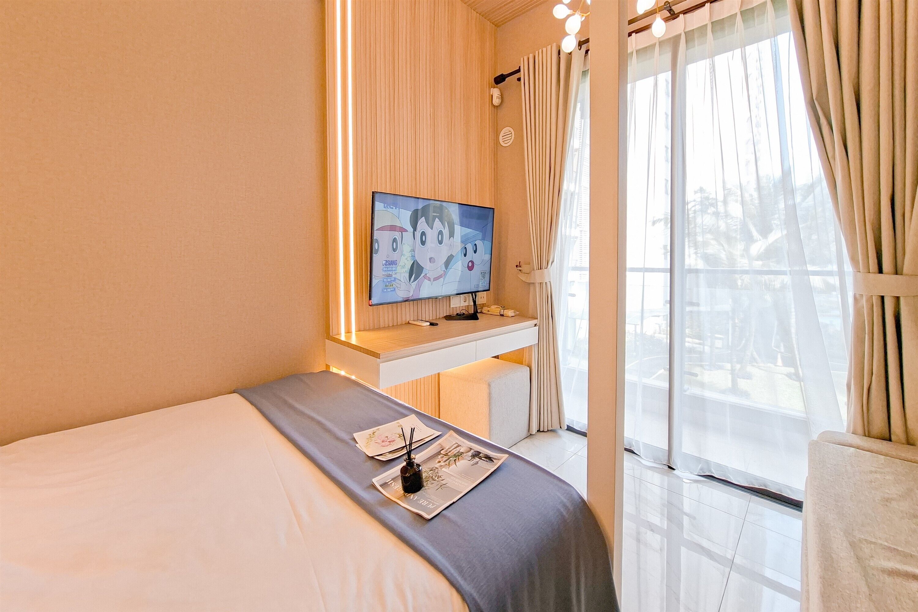 A hotel room with a bed, a desk with a flat-screen TV, and a large window with curtains.