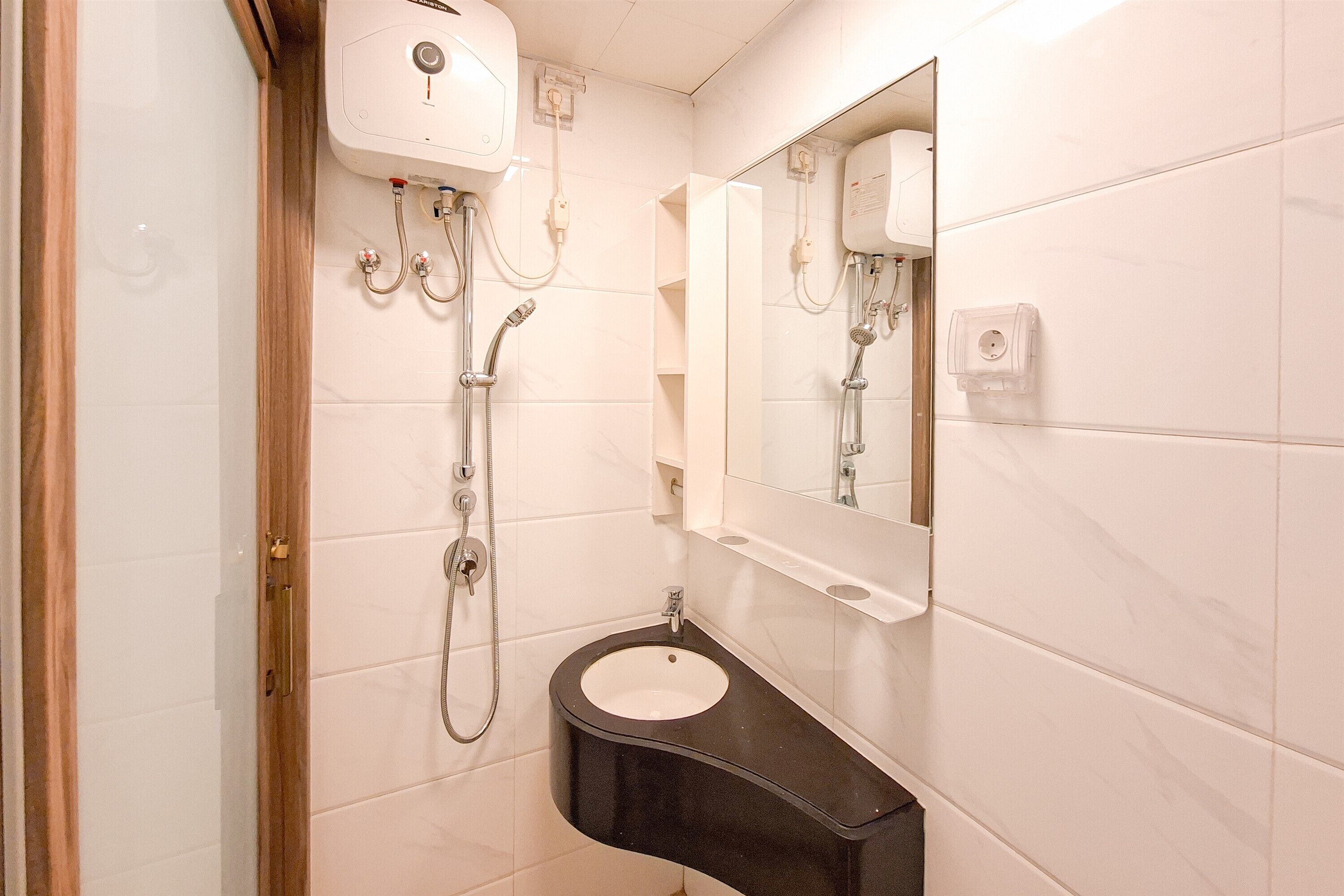 A bathroom with white tiled walls, a black sink, a mirror, and a shower with a handheld showerhead.
