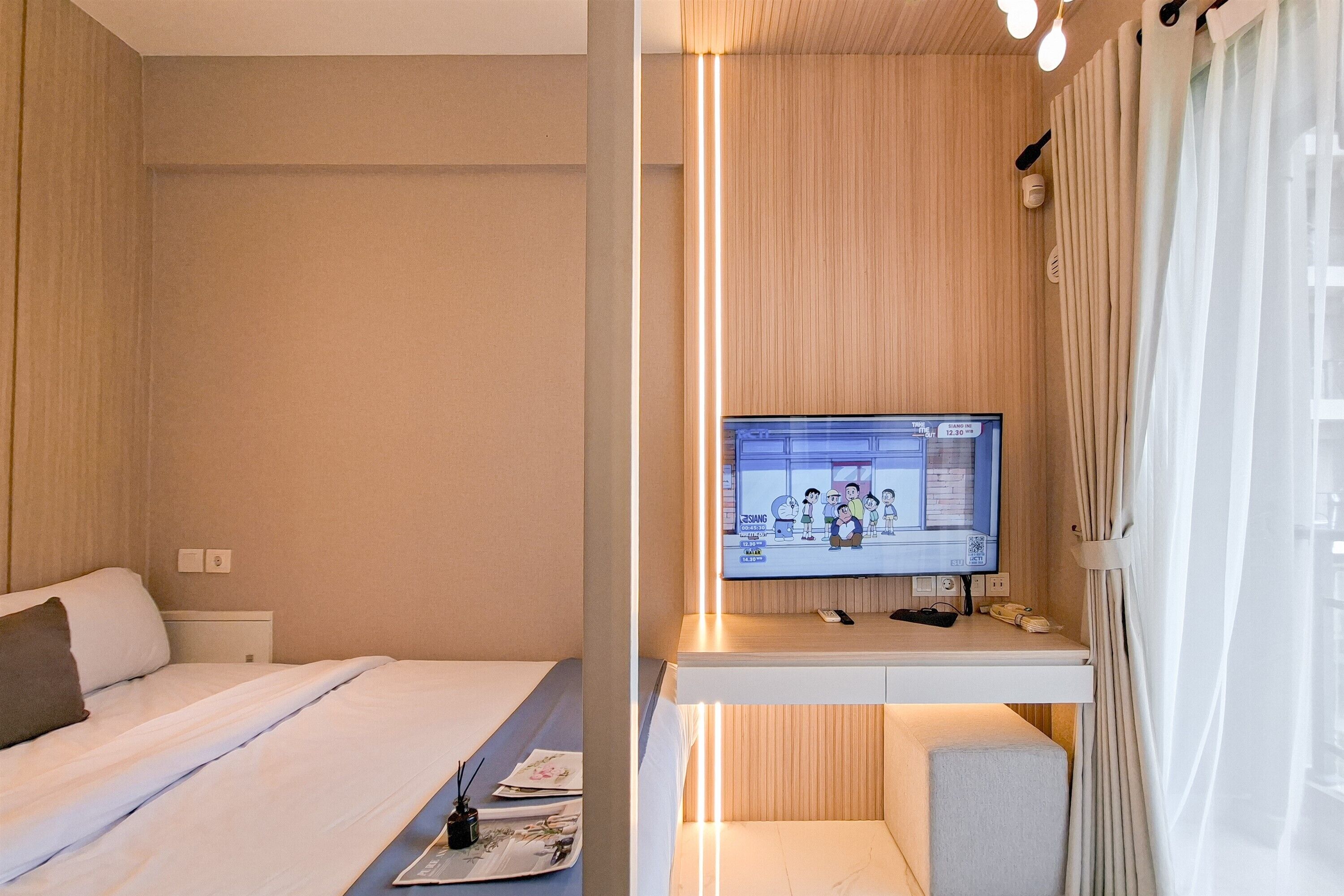 A hotel room with a bed, a desk with a TV, and a window with curtains.