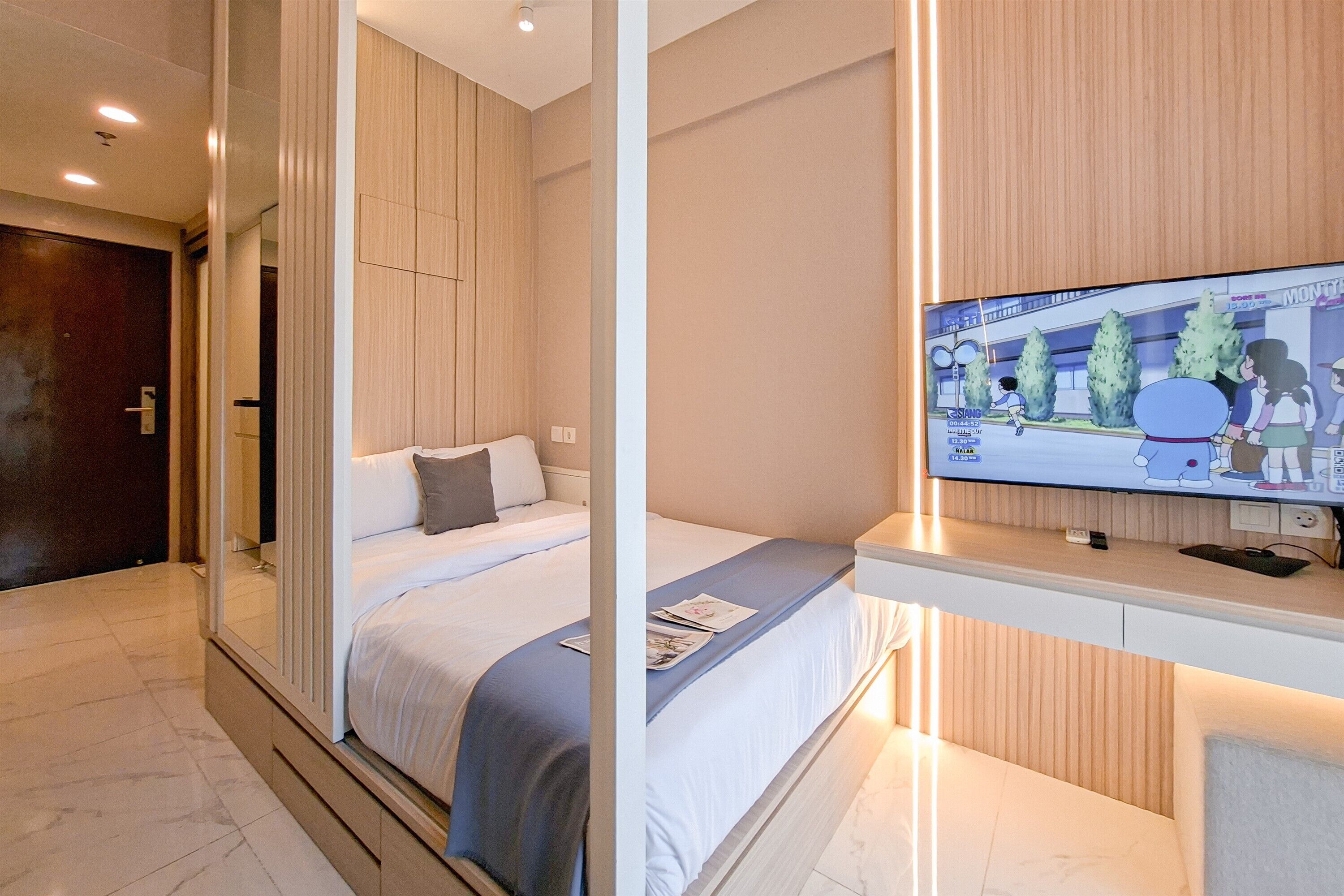 A modern hotel room with a large bed, a TV on a stand, and a wooden panel wall.