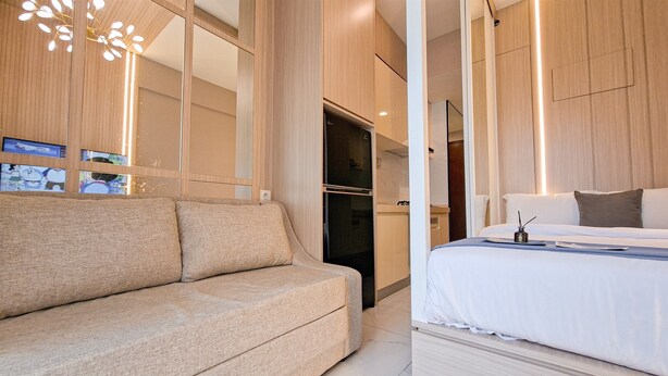 A modern hotel room with a sofa, a bed, a TV, and a kitchen area. - Elegant & Strategic Studio Room At Sky House Bsd Apartment (Pagedangan)