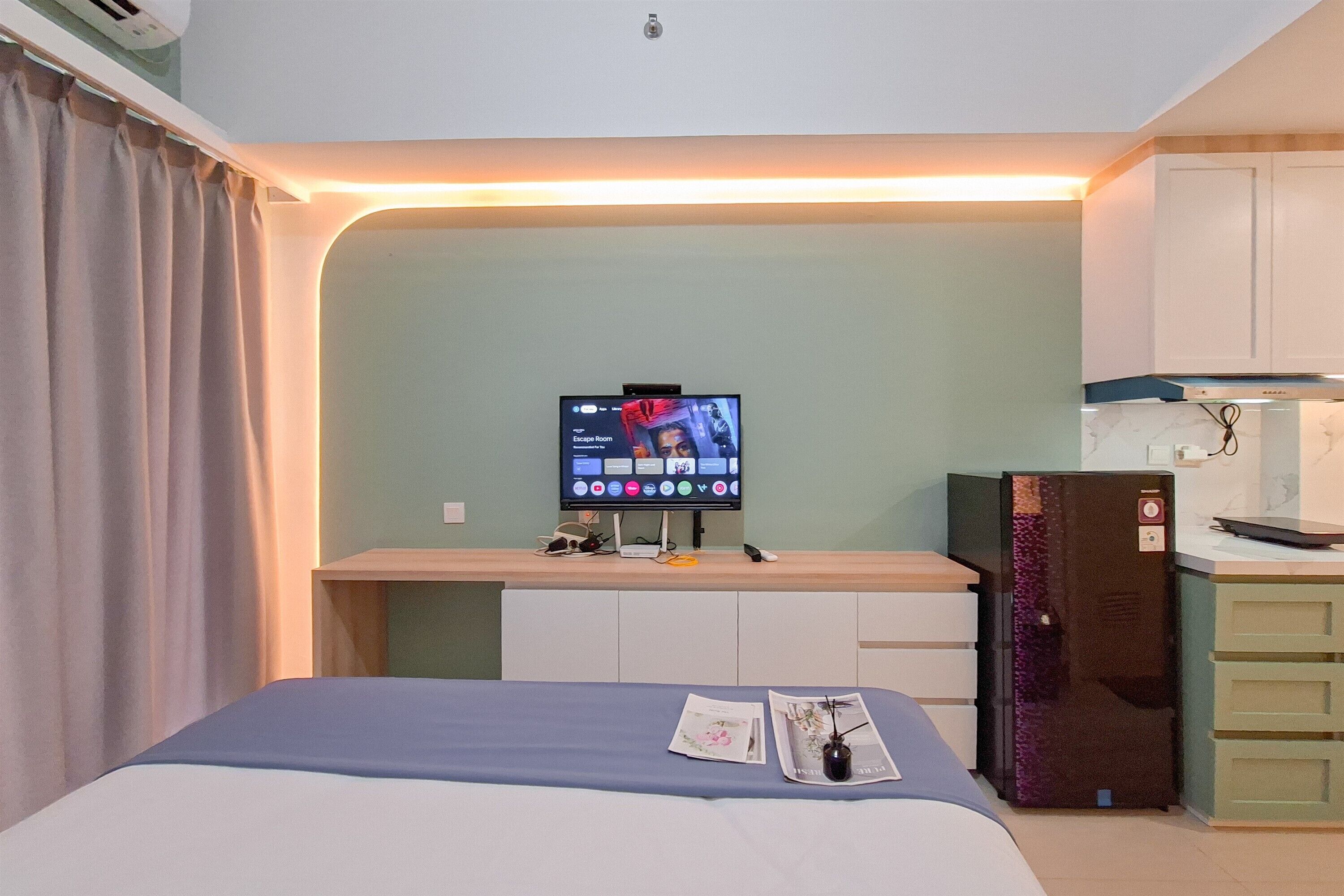 Una moderna camera d'albergo con un letto, una scrivania con un computer, un frigorifero e un angolo cottura.