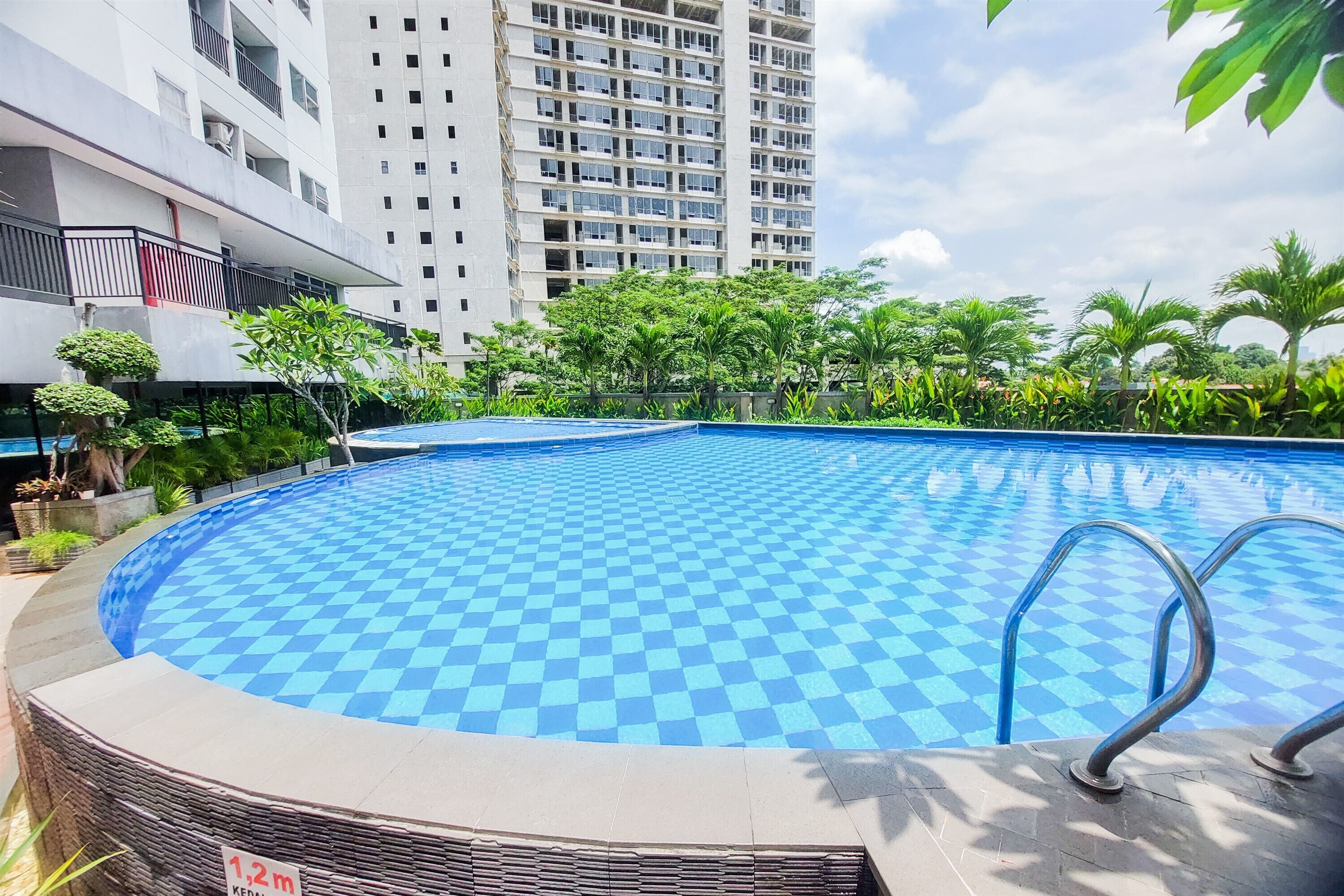 Ein Pool mit Schachbrettmuster, umgeben von Grünpflanzen und einem Hochhaus im Hintergrund.