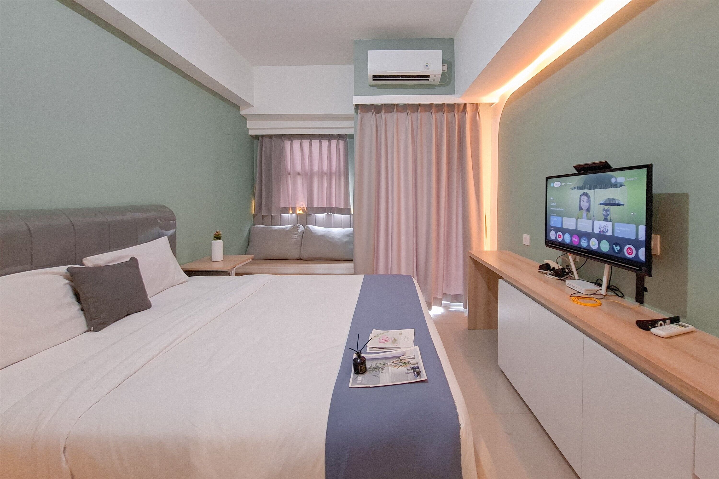 A hotel room with a large bed, a desk with a computer, and a TV on the wall.
