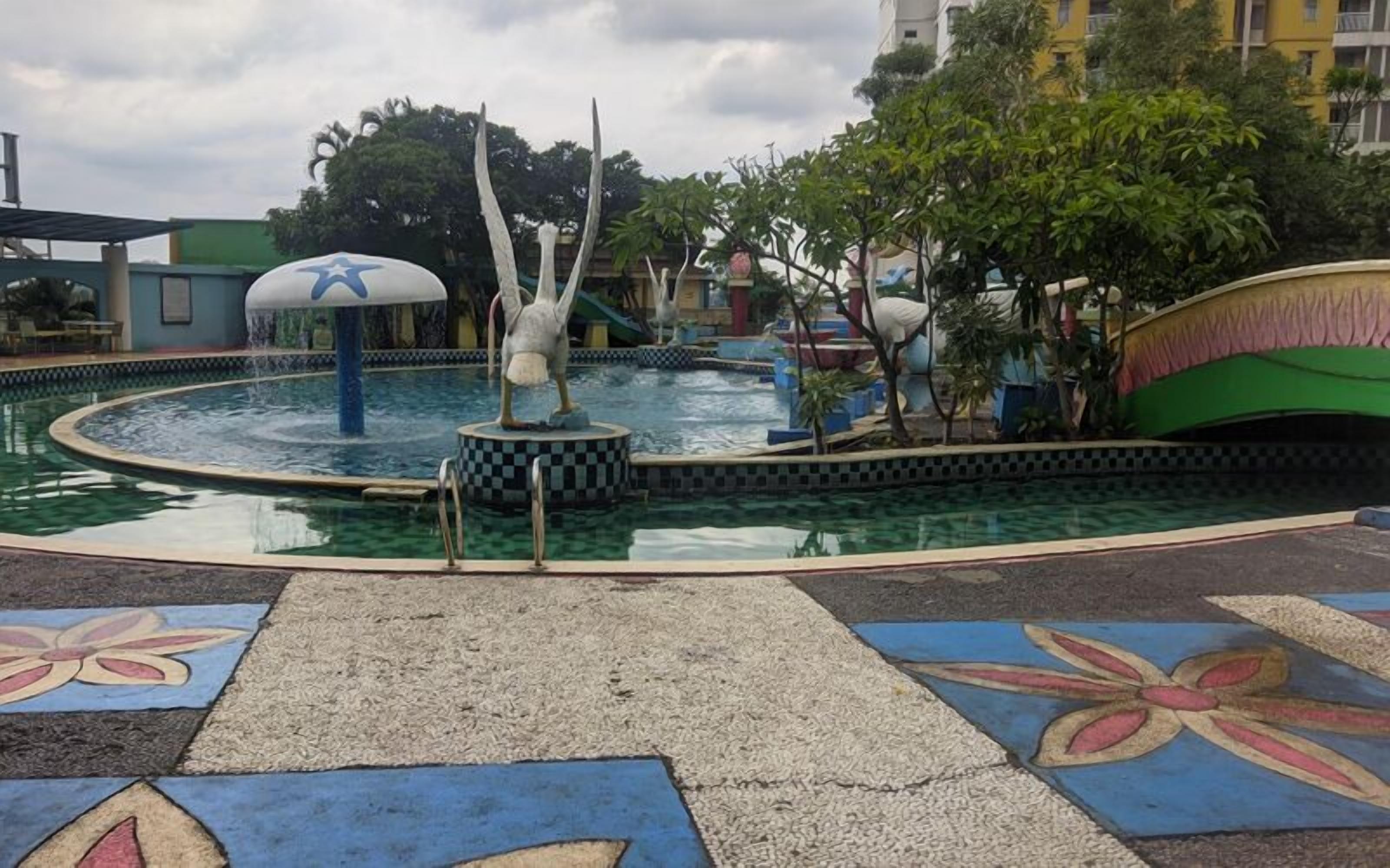 A swimming pool with a central fountain, surrounded by a tiled walkway with floral patterns.