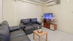 A living room with a dark leather sofa, a wooden coffee table, and a TV on a stand. - Combined 1Br With Extra Room Apartment At Green Pramuka City (Jakarta)