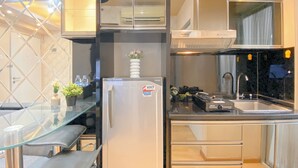 A compact kitchen with a refrigerator, sink, and a glass-top dining table. - 2Br Near Baywalk Mall Apartment At Green Bay Pluit (Jakarta)