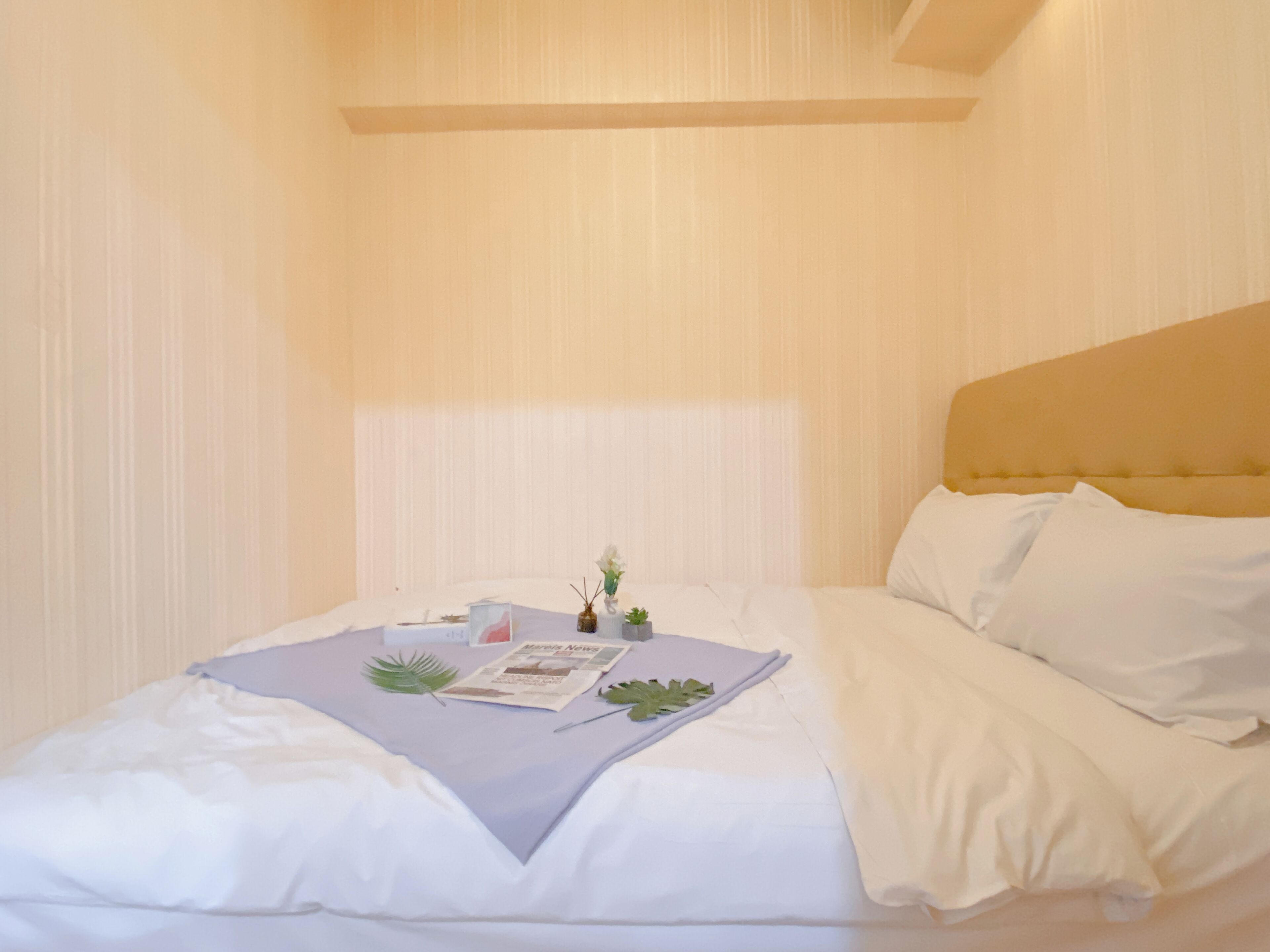 Un letto rifatto con lenzuola bianche, un comodino con una pianta e una rivista sul letto.