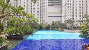 A swimming pool surrounded by lush greenery and tall residential buildings. - 2Br Near Baywalk Mall Apartment At Green Bay Pluit (Jakarta)