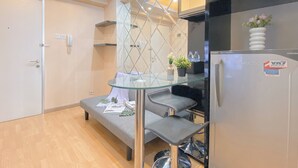 A modern kitchen with a glass-top dining table, grey bar stools, and a refrigerator with a Toshiba logo. - 2Br Near Baywalk Mall Apartment At Green Bay Pluit (Jakarta)