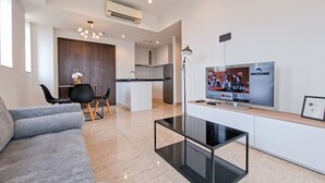 A modern living room with a grey sofa, a glass coffee table, and a TV displaying a sports event. - Modern Contemporary Cozy 2Br At Branz Bsd City Apartment (Pagedangan)