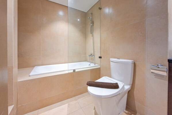 Un baño moderno con ducha envuelta en vidrio, una bañera blanca y un inodoro con una toalla.
