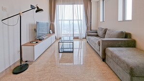 A modern living room with a sofa, a coffee table, a TV on a stand, and a floor lamp. - Modern Contemporary Cozy 2Br At Branz Bsd City Apartment (Pagedangan)