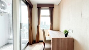 A modern hotel room with a wooden desk, a chair, and a potted plant. - Modern Minimalist Studio (No Kitchen) At Great Western Apartment (Tangerang)