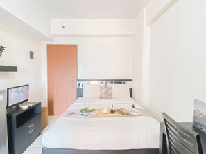 A hotel room with a bed, a desk with a computer, a door, and a wall-mounted TV. - Minimalist Studio Apartment At Margonda Residence 2 (Depok)