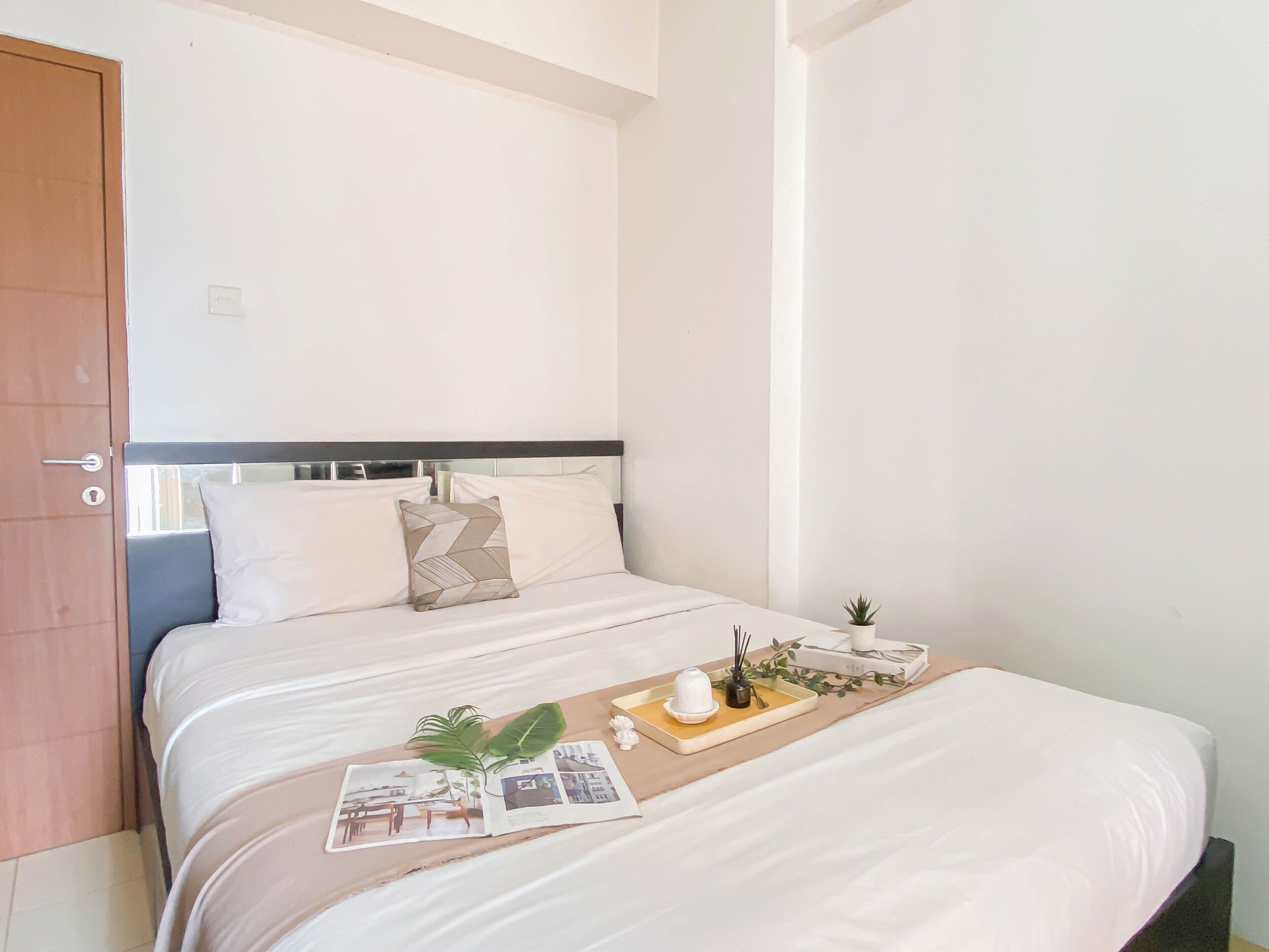 Una cama bien hecha con cabecera, una pequeña planta en maceta y una bandeja con una taza y un libro sobre la cama.