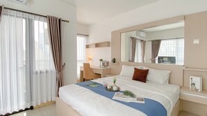 A hotel room with a large bed, a desk, a chair, and a window with curtains. - Scandinavian Minimalist 2Br At Tamansari Semanggi Apartment (Jakarta)