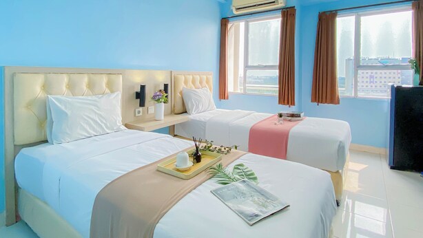 Une chambre d’hôtel avec deux lits, une grande fenêtre avec des rideaux, un appareil de climatisation et une vue sur les bâtiments environnants.