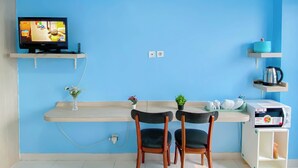 Eine kleine Küchenzeile mit Mikrowelle, Wasserkocher und Regalen mit Küchenutensilien. Ein Fernseher ist an der Wand montiert und es gibt zwei Stühle an einem Tisch.