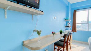 Ein modernes Hotelzimmer mit einem an der Wand befestigten Flachbildfernseher, einem Holztisch mit Blumenvase, einem Sessel und einem Fenster mit Blick auf Gebäude.