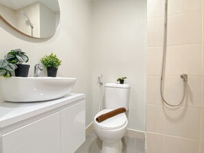 A bathroom with a white sink, two potted plants, a toilet with a towel on the seat, and a shower. - Studio Apartment At Meikarta Near Aeon Delta Mas (Cikarang)