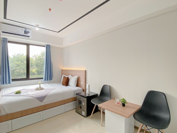 A hotel room with a bed, a desk, a chair, an air conditioner, and a window with curtains. - Studio Apartment At Meikarta Near Aeon Delta Mas (Cikarang)