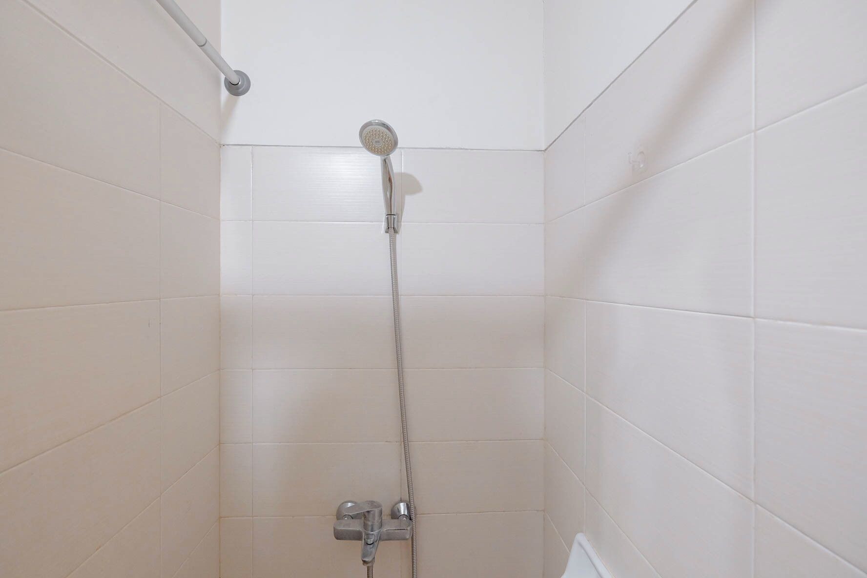 A shower with a handheld showerhead and a wall-mounted faucet in a tiled bathroom.