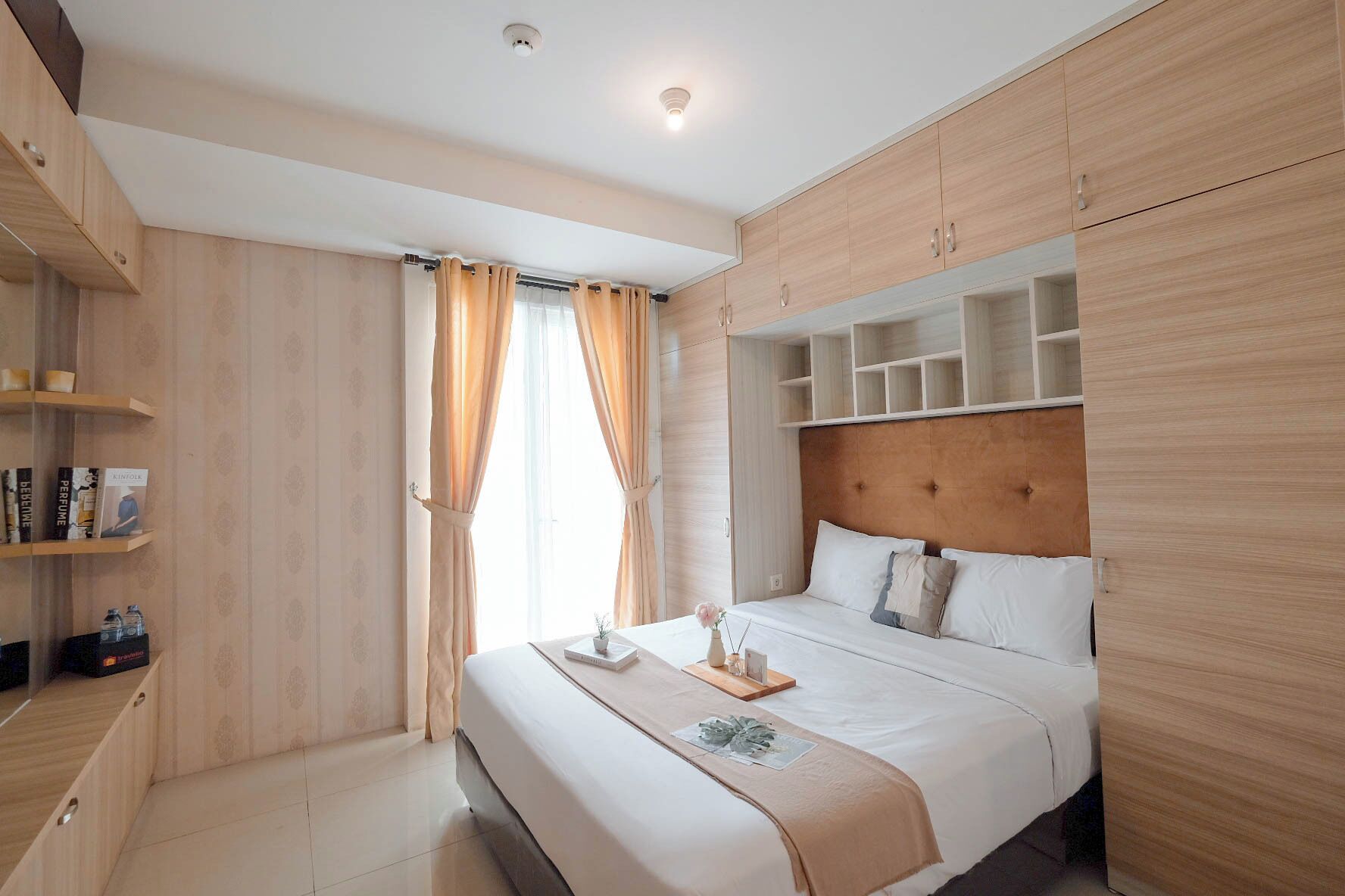 A modern hotel room with a large bed, wooden headboard, built-in shelving, and a window with curtains.