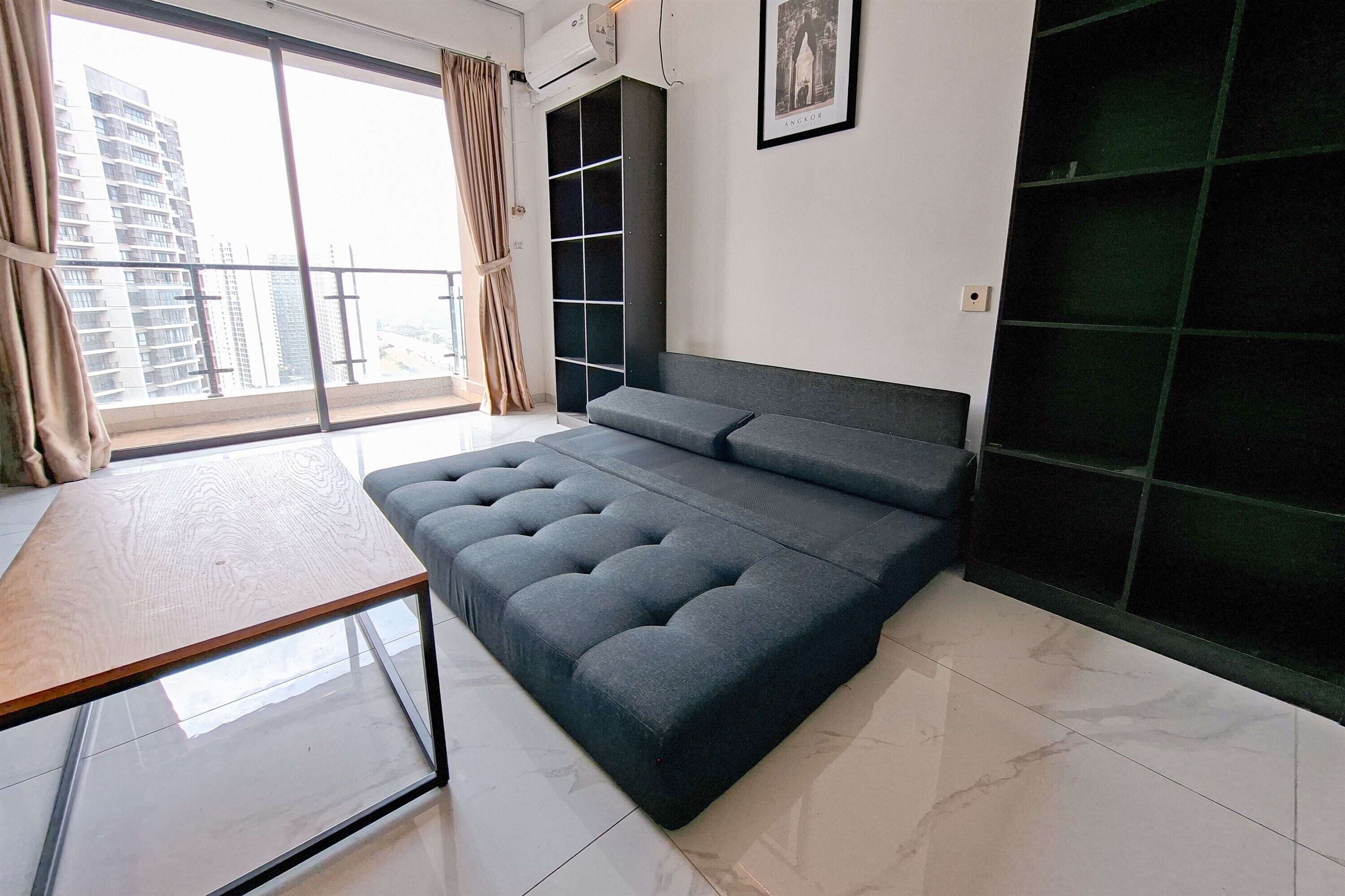 A modern bedroom with a large bed, a glass coffee table, a wardrobe, and a view of a cityscape.