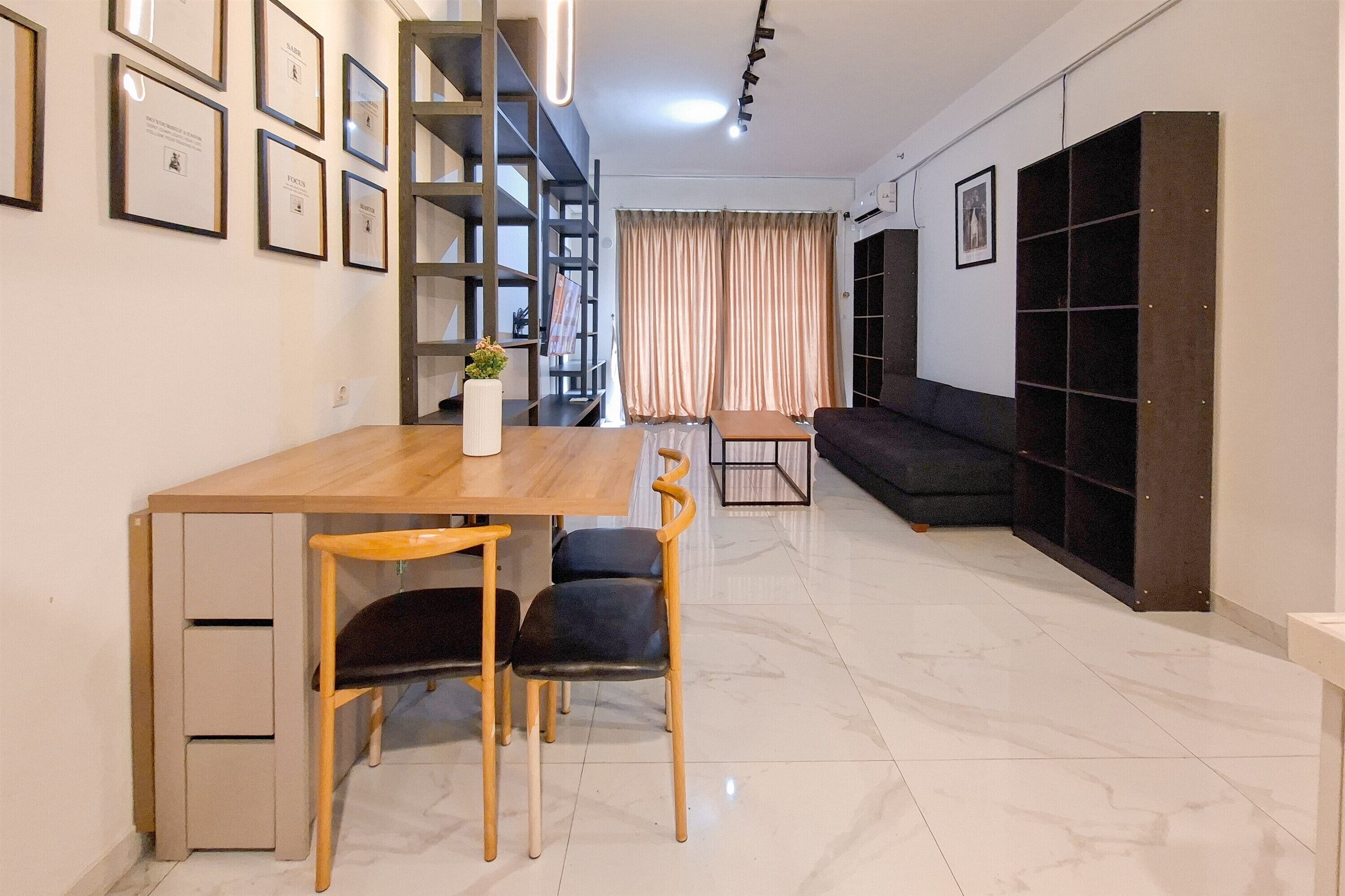 A modern living room with a wooden dining table, two chairs, a sofa, a bookshelf, and a staircase.