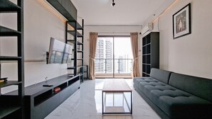 Uma sala de estar moderna com televisão de tela plana, um sofá cinza, uma mesa de centro de vidro e uma janela grande com cortinas.