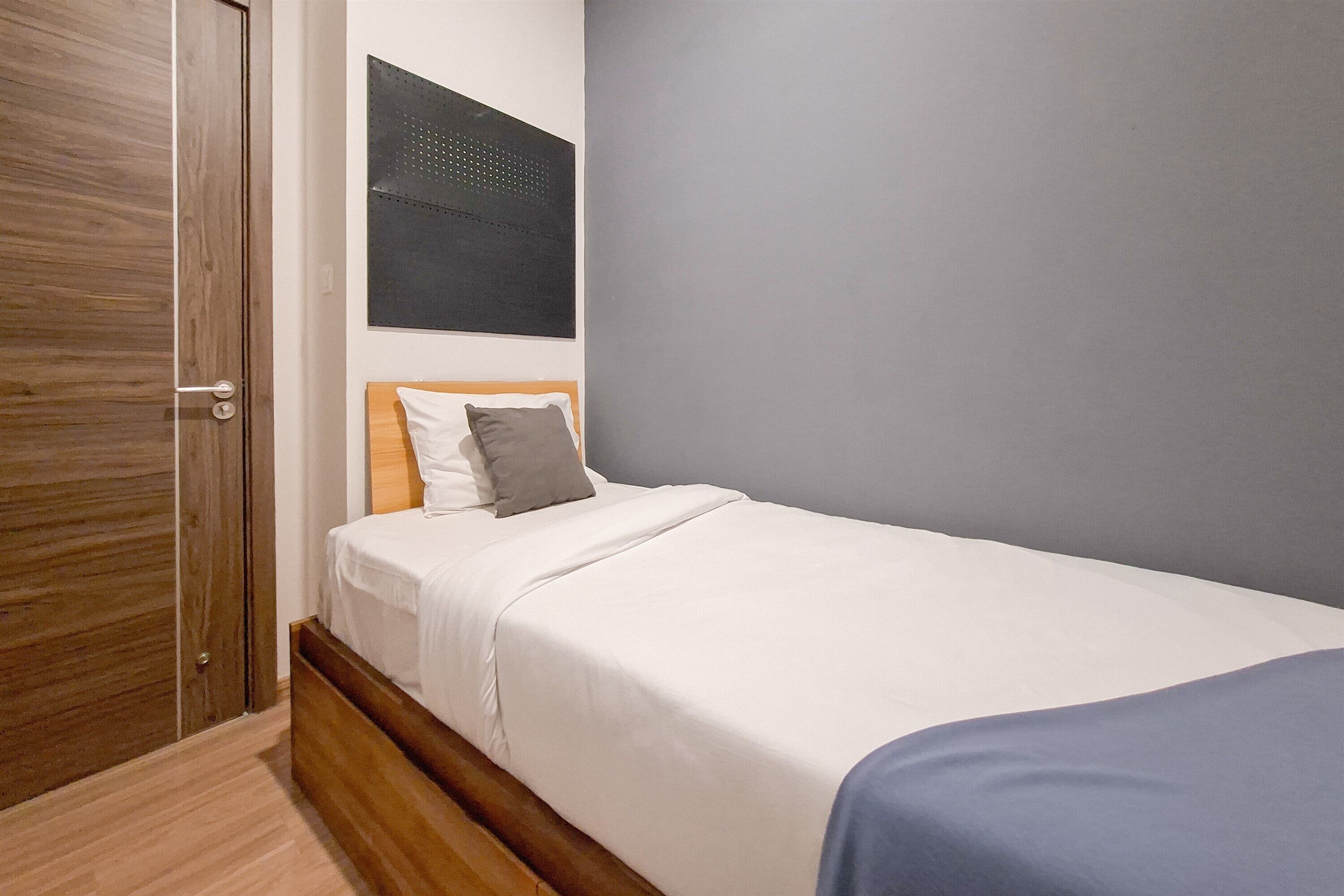 A bedroom with a wooden door, a bed with white bedding, a gray pillow, and a gray wall.