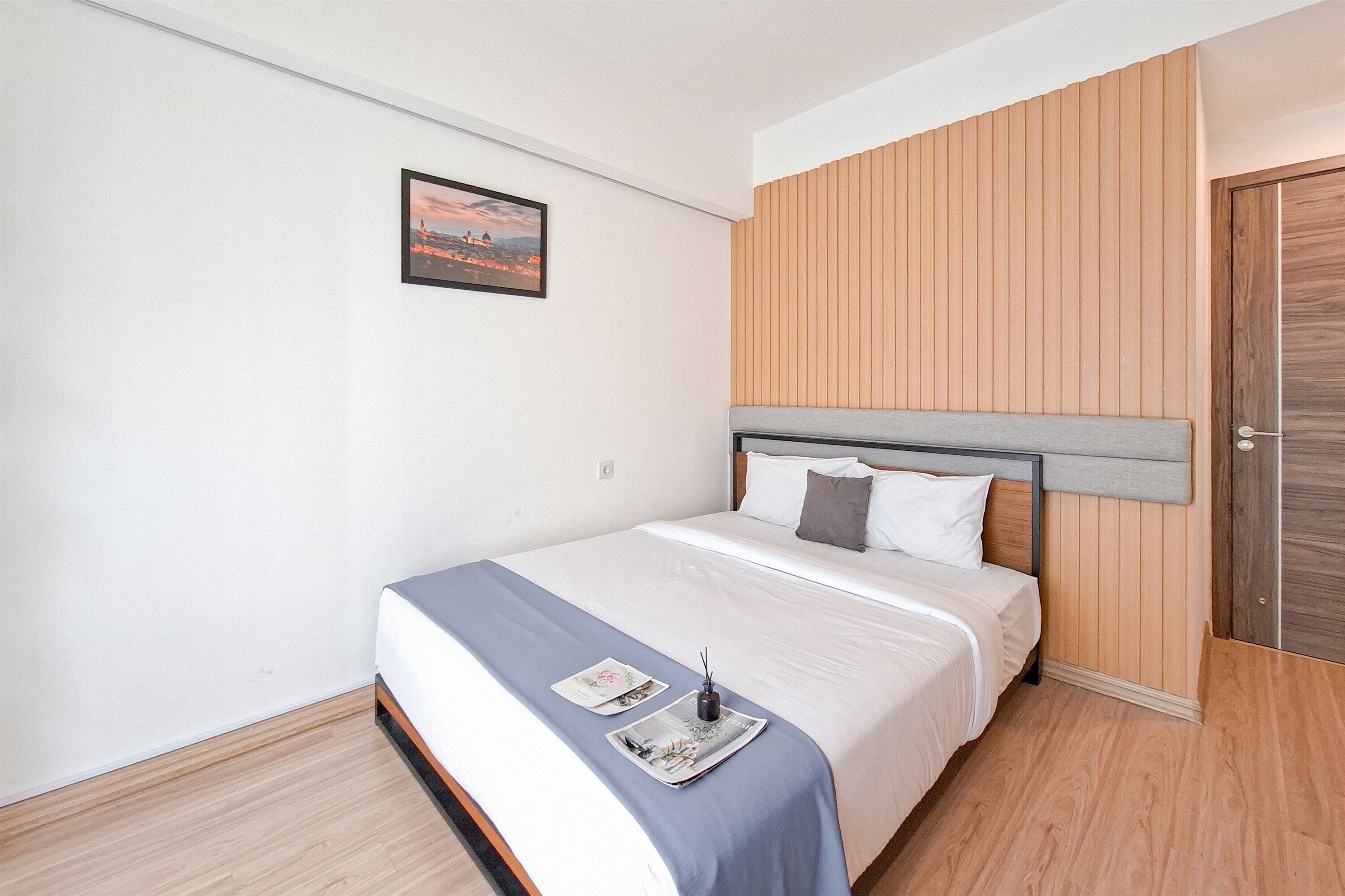 Un lit bien fait, avec une tête de lit, un tableau encadré accroché au mur et une porte en bois.