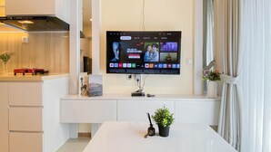 Eine moderne Küche mit Wand-Fernseher, einem weißen Esstisch und einem kleinen Topf mit Pflanze.