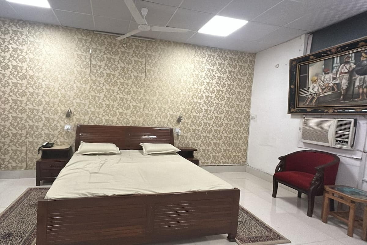 A bedroom with a wooden bed, a nightstand, a red chair, a small table, and a wall-mounted air conditioner.