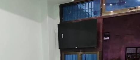 Een kamer met een enkel bed, een airconditioner, een raam met een blauw gordijn en een kleine plant aan de muur.