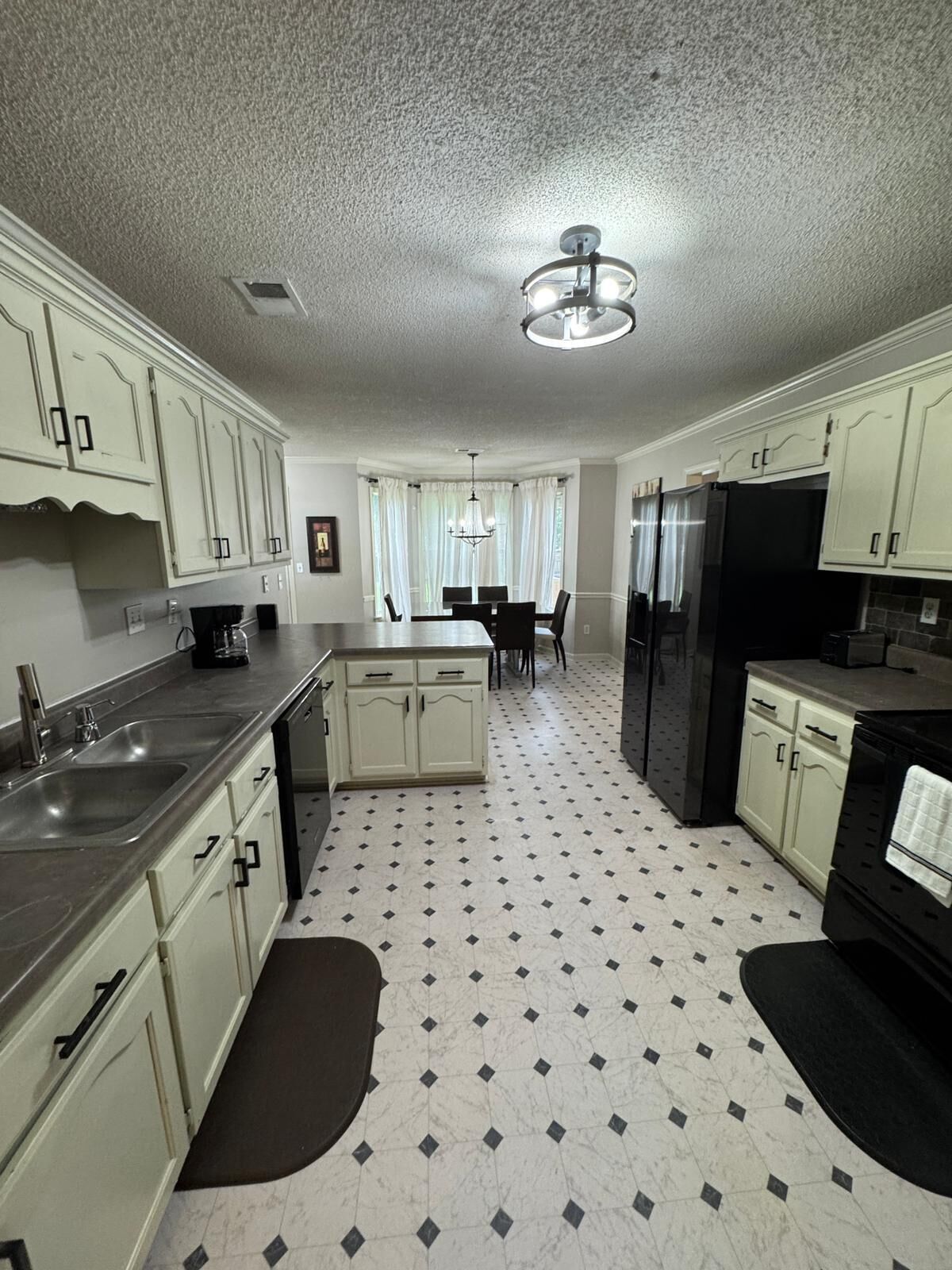 A kitchen with white cabinets, a black refrigerator, a dining table with chairs, and a chandelier.