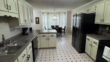 A kitchen with white cabinets, a black refrigerator, a dining table with chairs, and a chandelier.