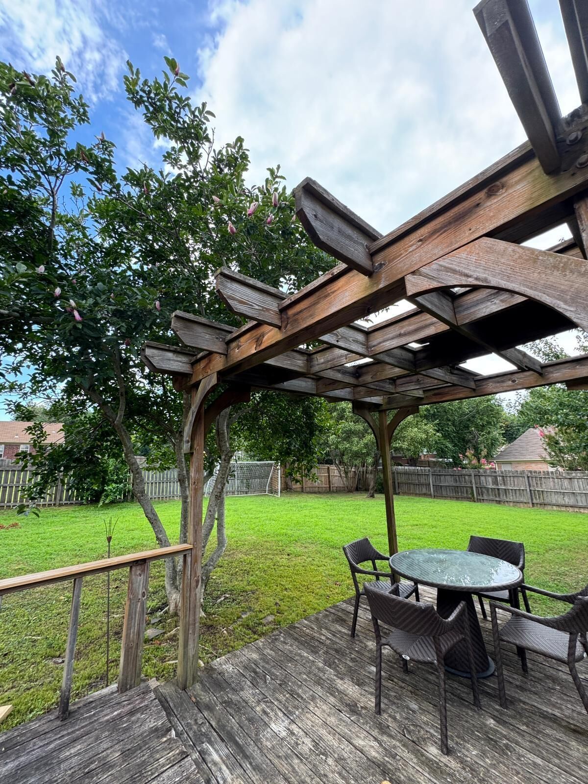 Een houten terras met een pergola, zitplaatsen buiten en een gazon.