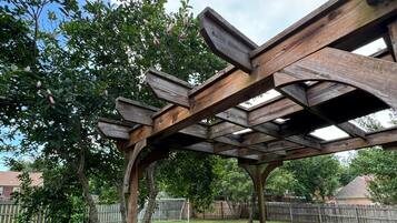 Een houten terras met een pergola, zitplaatsen buiten en een gazon.