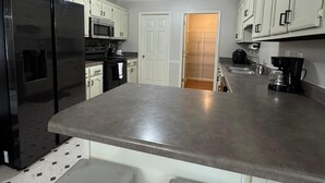 A modern kitchen with white cabinets, a black refrigerator, a microwave, and a coffee maker. - Cozy 5BR / 2.5BA- Brick Home in Olive Branch (Olive Branch)
