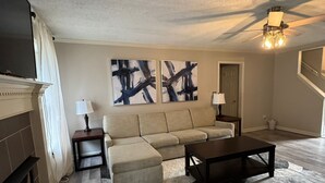 A living room with a sectional sofa, a coffee table, a fireplace, and abstract wall art. - Cozy 5BR / 2.5BA- Brick Home in Olive Branch (Olive Branch)