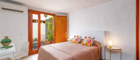 A bedroom with a bed, a desk, a chair, and a potted plant.