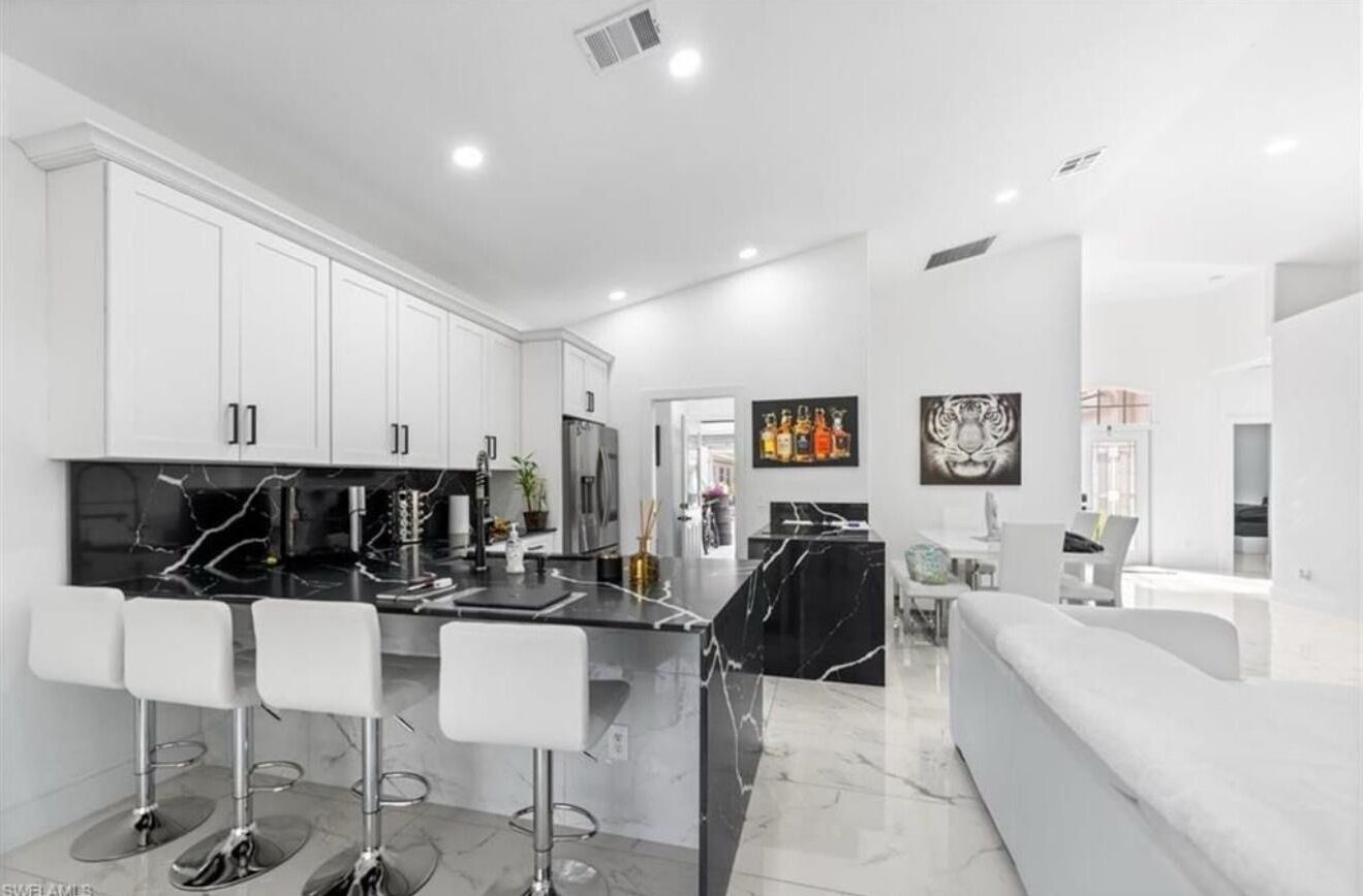 A modern kitchen with white cabinets, a black marble island, and four bar stools.