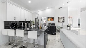A modern kitchen with white cabinets, a black marble island, and four bar stools. - Modern Naples Home | Golf Course • Heated Pool & Spa (Naples)